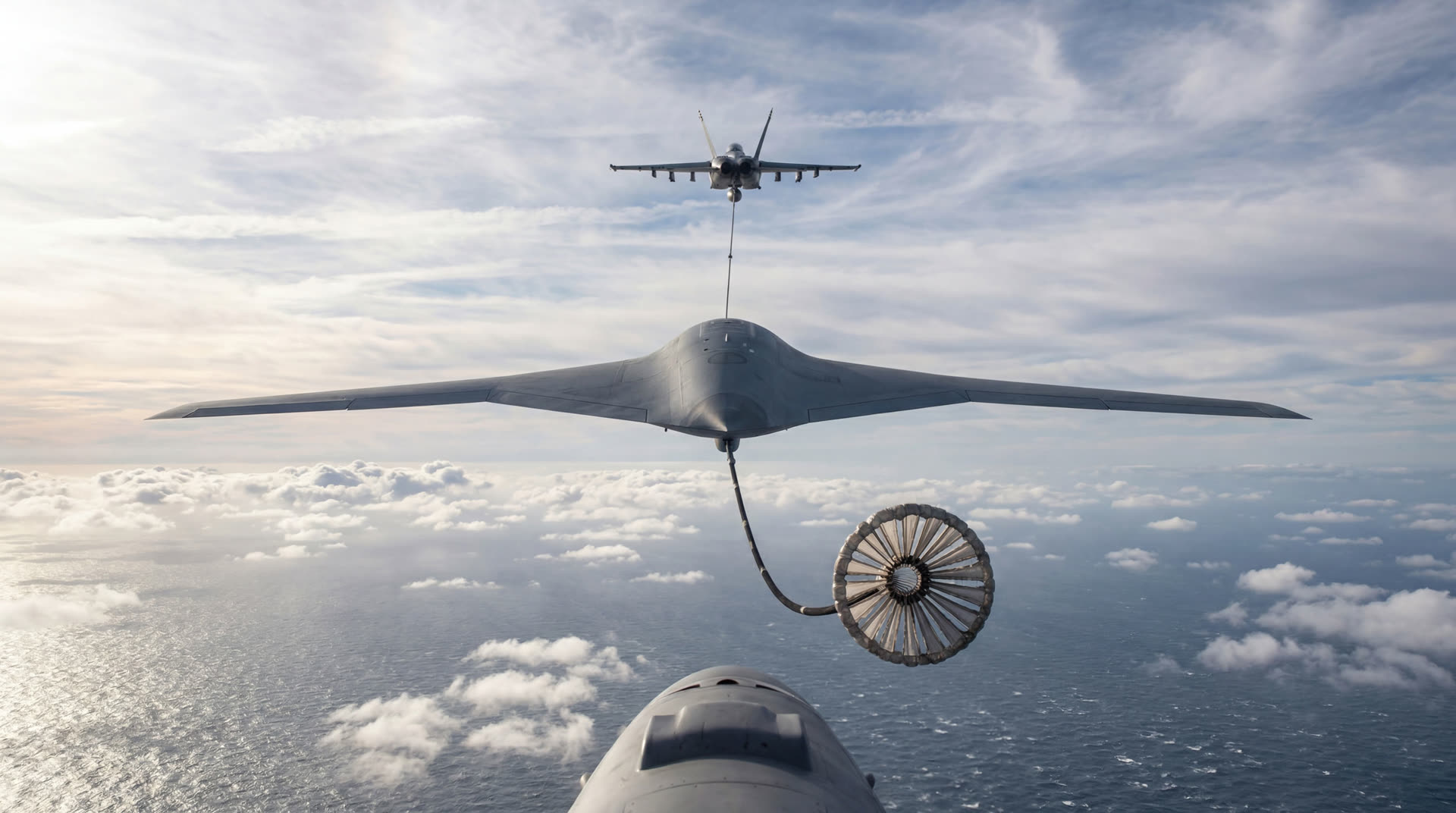 F-18 towing a flying wing with refueling drogue over the ocean